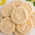 Close-up of soft, chewy lemon cookies coated in sugar with fresh lemon slices, showcasing a delicious lemon cookies recipe. One cookie has a bite taken out of it.