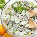 A glass bowl filled with a fresh Creamy Cucumber Salad mixed with red onions and topped with fresh dill