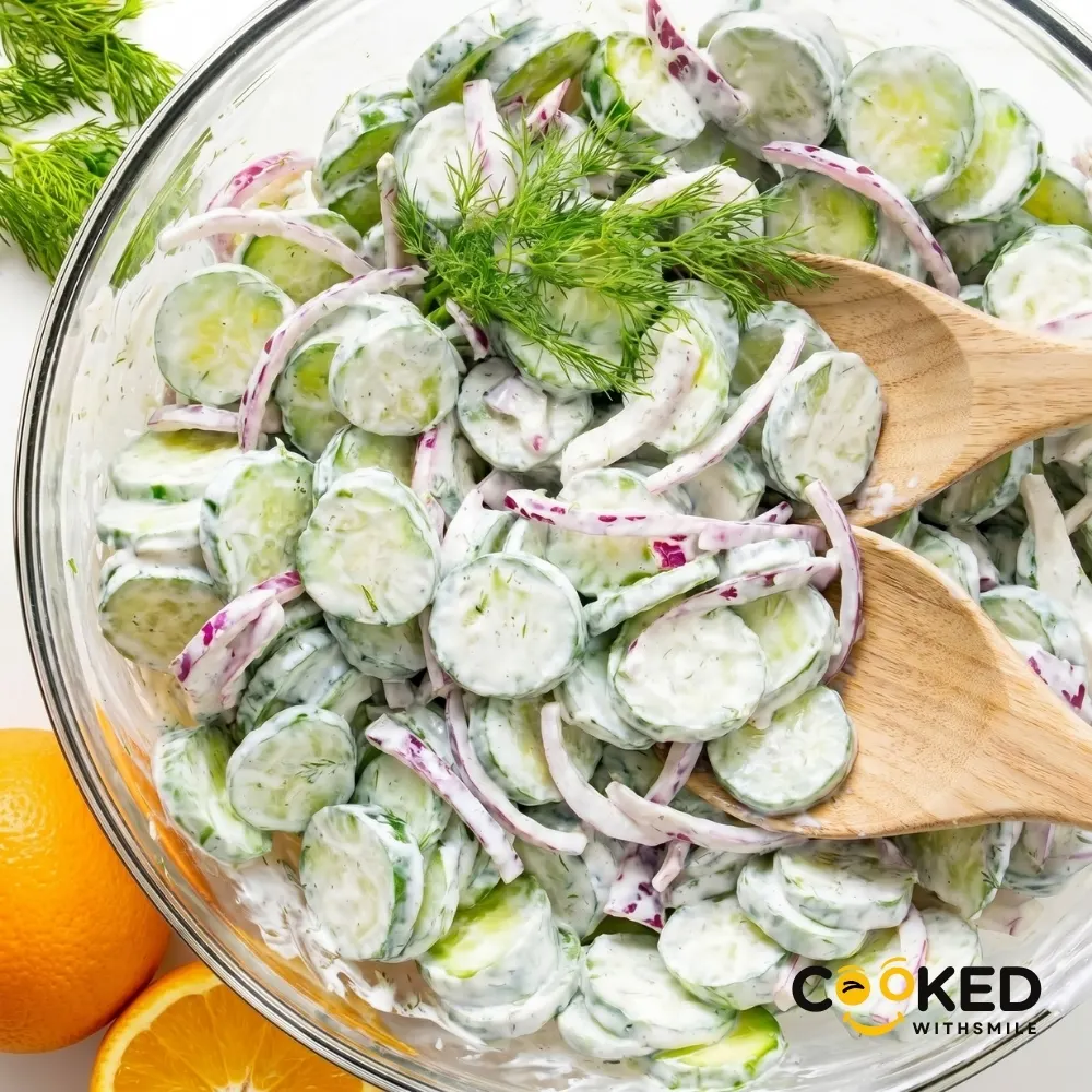 A glass bowl filled with a fresh Creamy Cucumber Salad mixed with red onions and topped with fresh dill