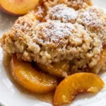 A close-up view of a portion of peach cobbler dump cake on a white plate, highlighting the tender peach slices and golden crumble topping.